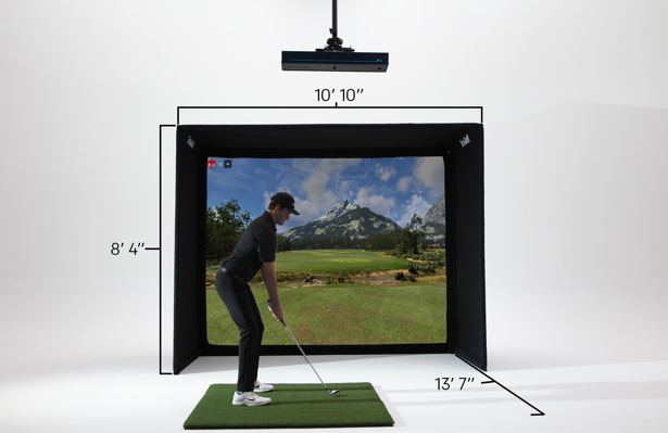 A golf simulator setup shown in a studio with dimension labels: a black enclosure, a suspended impactor, a green turf mat, and a golf course scene displayed on the screen. A person is visible inside the simulator, and measurement lines annotate the enclosure dimensions.